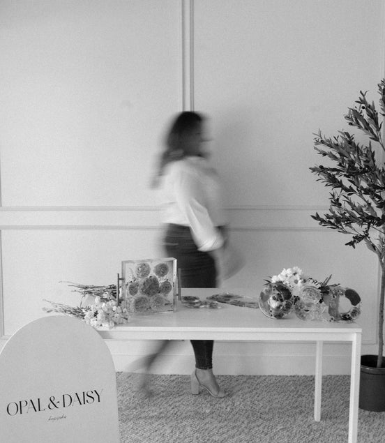 Person walking past a table with floral arrangements and 'Opal & Daisy' branding in a room.