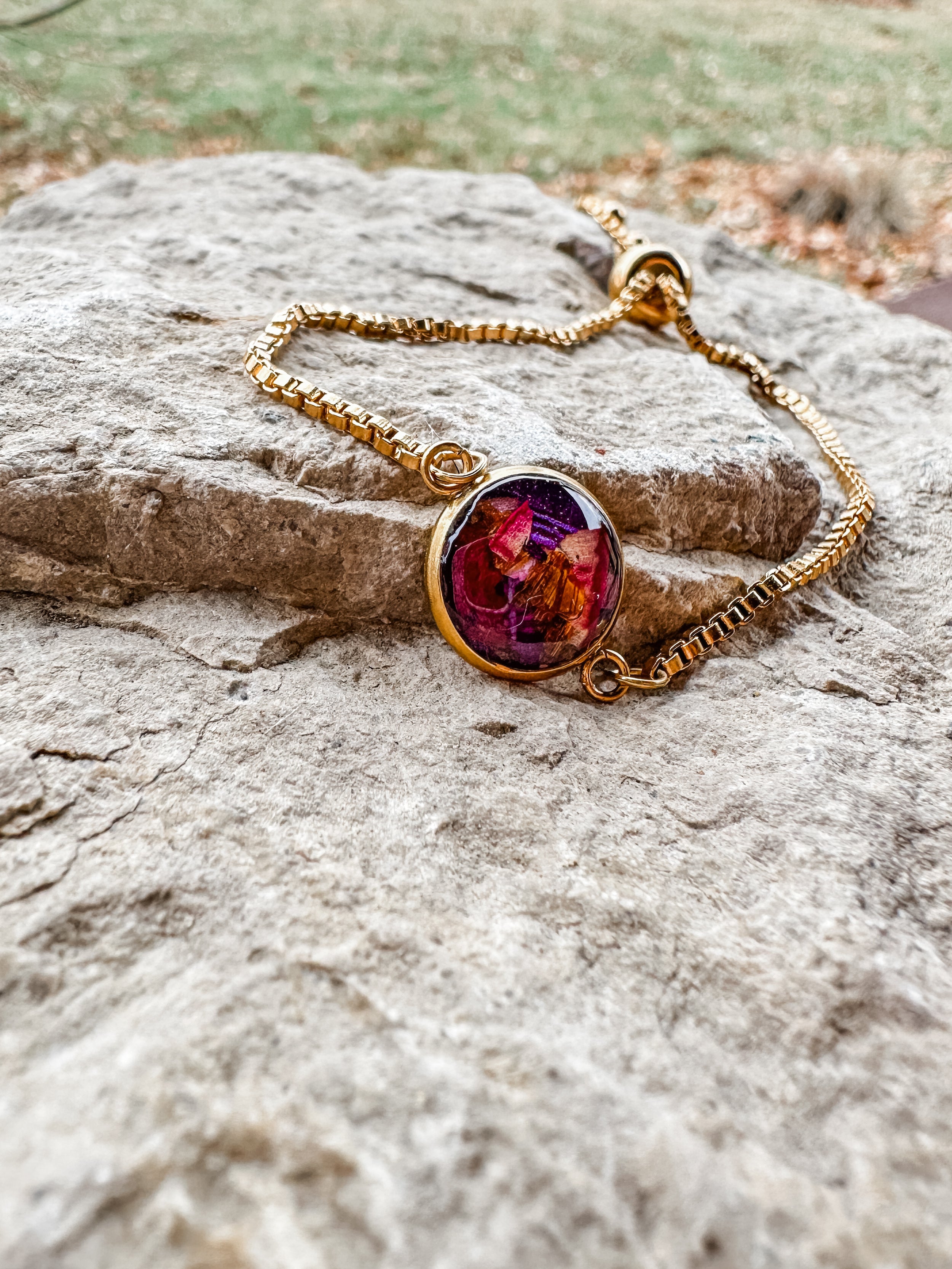 Gold bracelet with a colorful gemstone on a stone surface