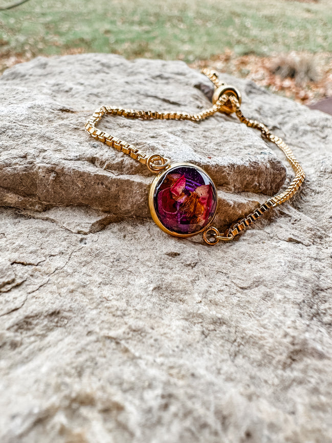 Gold bracelet with a colorful gemstone on a stone surface