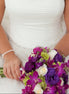 Bride in a white dress holding a bouquet of purple and green flowers.