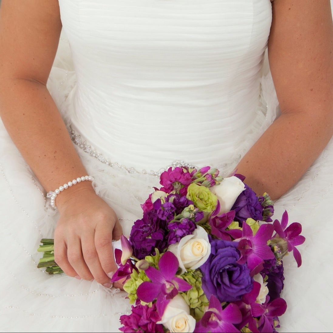 Bride in a white dress holding a bouquet of purple and green flowers.