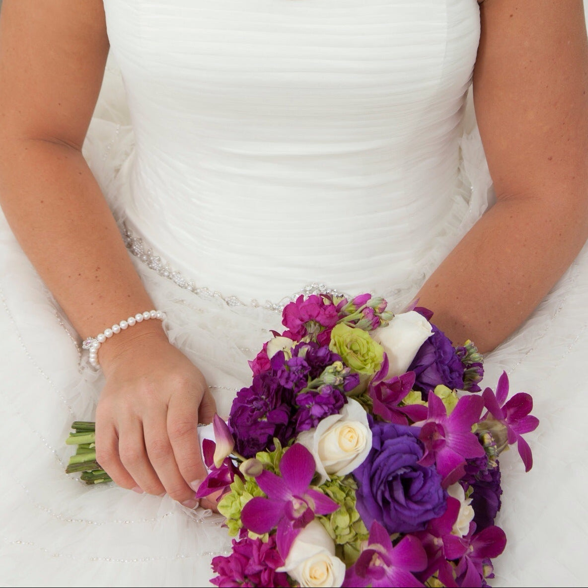 Bride in a white dress holding a bouquet of purple and green flowers.
