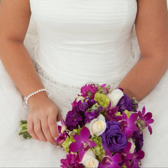 Bride in a white dress holding a bouquet of purple and green flowers.